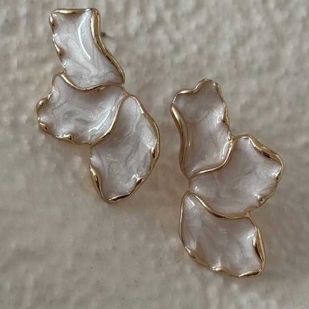 نمای نزدیک از گوشواره میخی با فرم نامنطم و لعاب و صدفی مرمرین و لبه های طلایی.