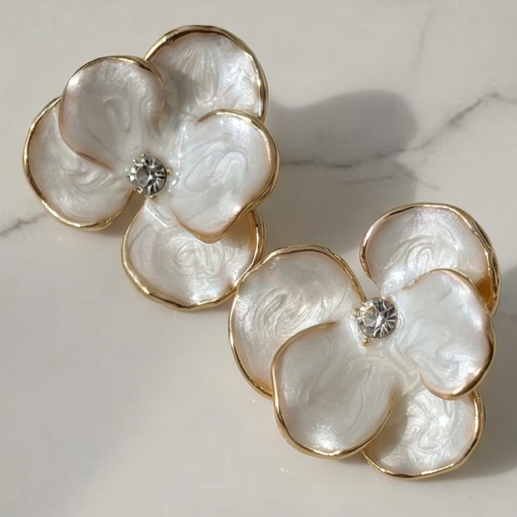 نمای نزدیک گوشواره میخی طرح گل پرپَر سفید صدفی با لبههای طلایی و نگین درخشان در مرکز.