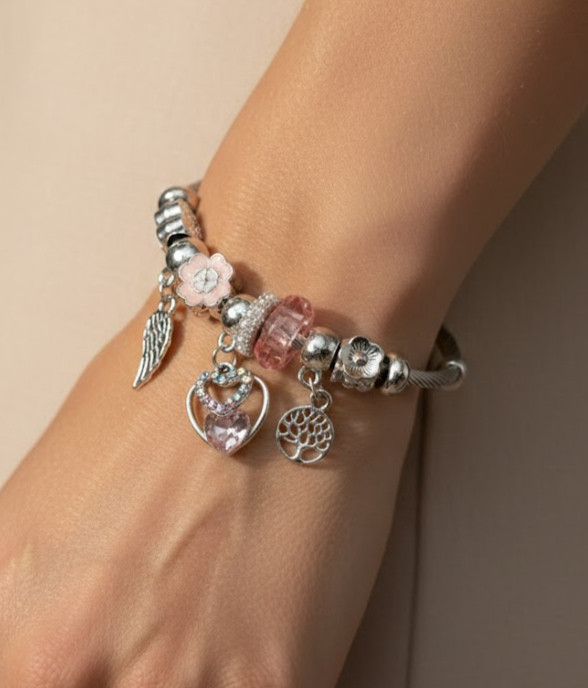 نمای نزدیک دستبند پاندورا نقرهای با آویزهای درخت زندگی، قلب و بال فرشته روی مچ دست مدل.