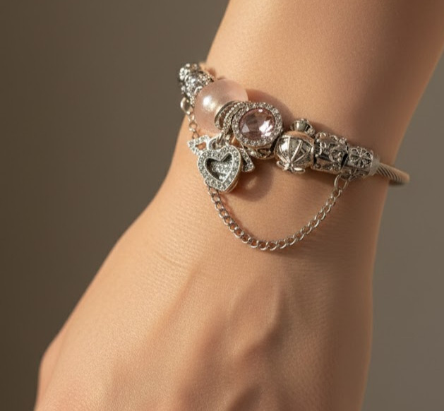 نمای نزدیک دستبند پاندورا نقرهای با زنجیر آویز ظریف و چارم قلب روی مچ دست مدل.