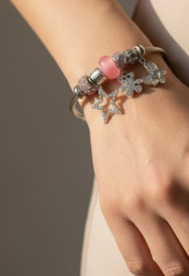 نمای نزدیک دستبند پاندورا نقرهای با آویز ستاره بزرگ نگیندار و خرس تدی روی مچ دست مدل